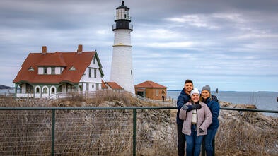 Adriana posando con su madre y hermano frente a un faro en Maine
